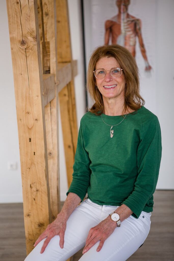 Tina Hirth sitzt in ihrer Praxis und lächelt. Sie hilft ihren Klienten zu mehr Energie zu kommen.